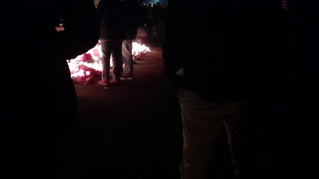 Kerzen auf dem Boden des Tatorts. Menschen im Dunkeln darum herum.